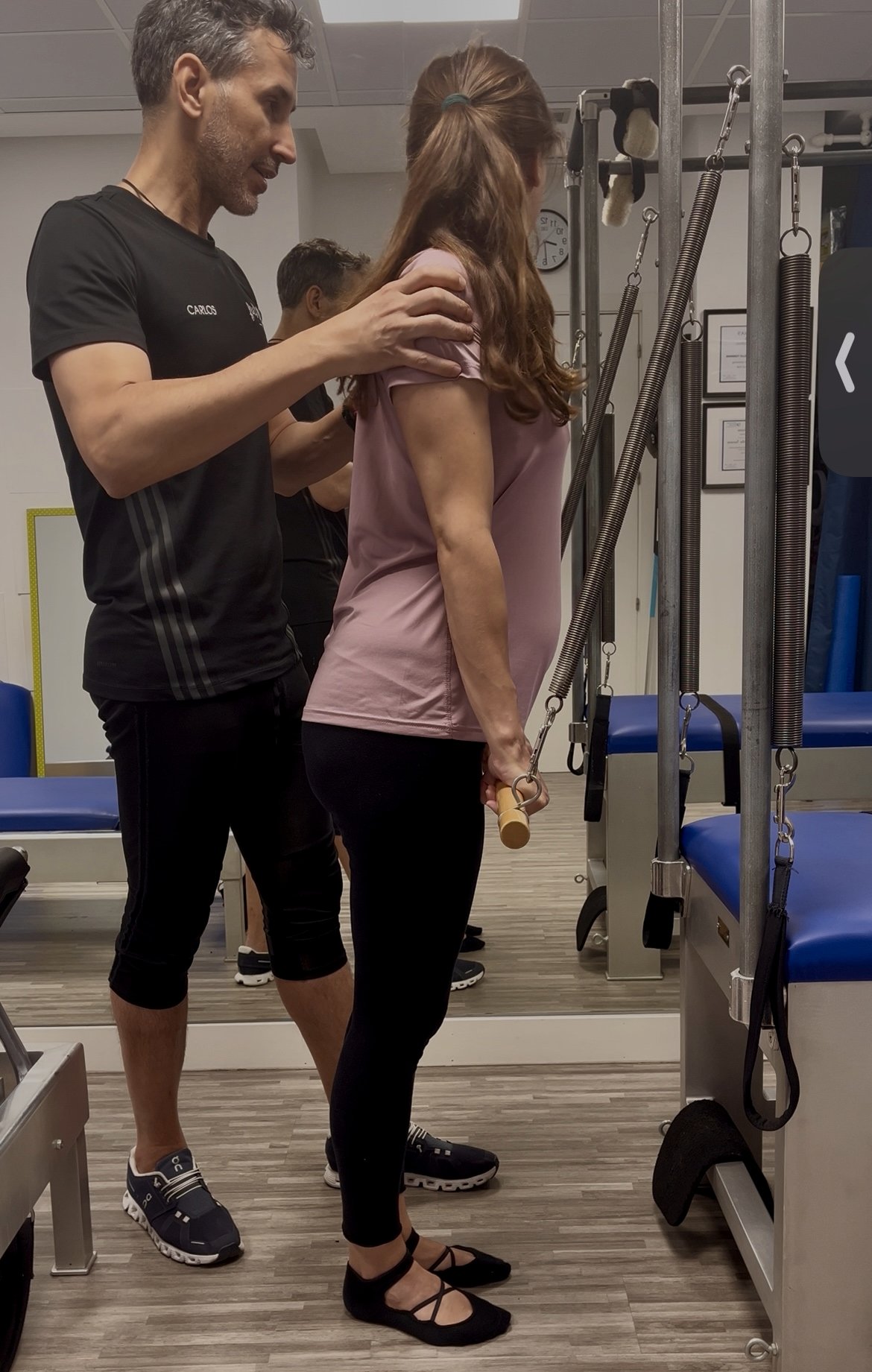 Instructor corrigiendo postura de una mujer embarazada durante una clase de Pilates en Cadillac en Feel Fit Madrid.